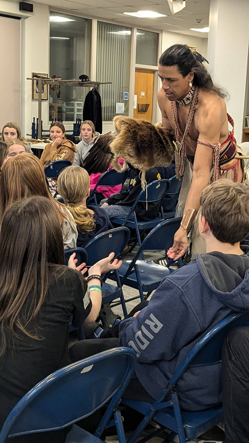 Annawon Weeden dressed in Native American traditional clothing interacting with students