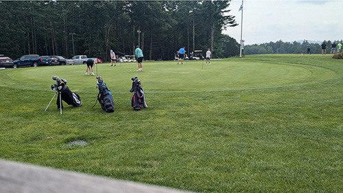 Three golf bags and golfers playing in the distance